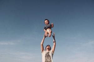 Photo of Man in Raising Baby Under Blue Sky